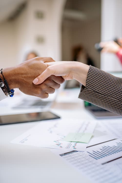 Two people shaking hands over trade and financial charts